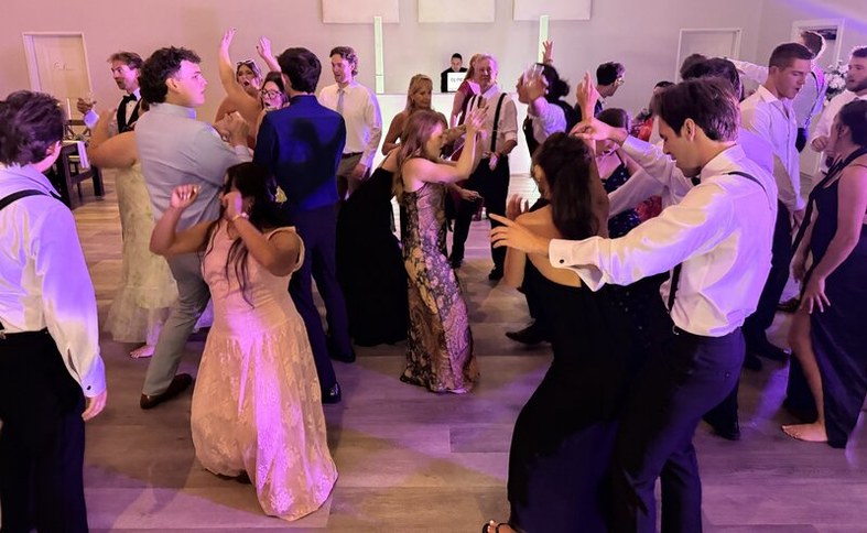 A packed dance floor of guests mid dance under soft purple lighting